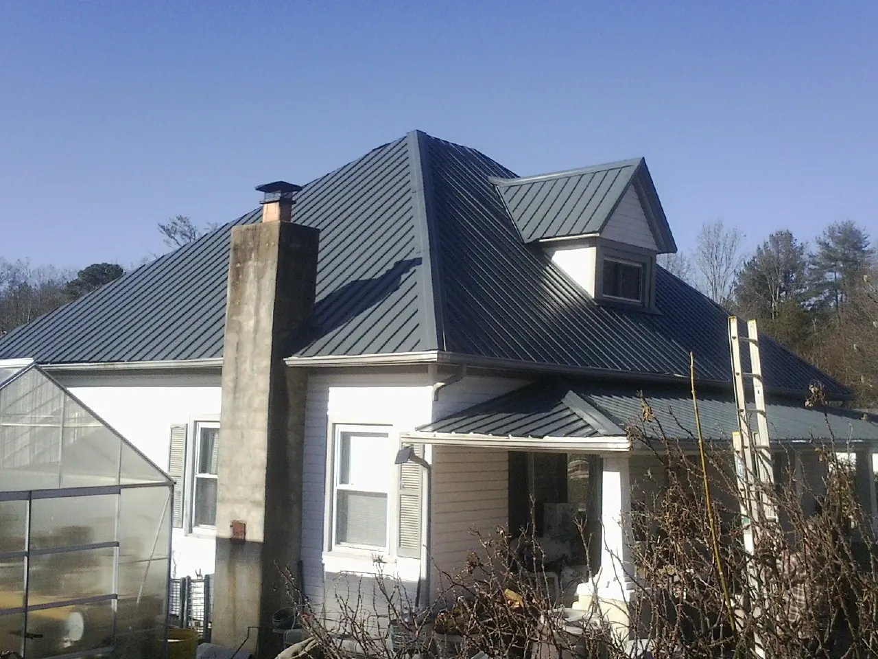 Dark blue standing seam metal roof on a white farmhouse with dormer — Slate & Tile Roof Repair by Roofing Brothers in Ahoskie