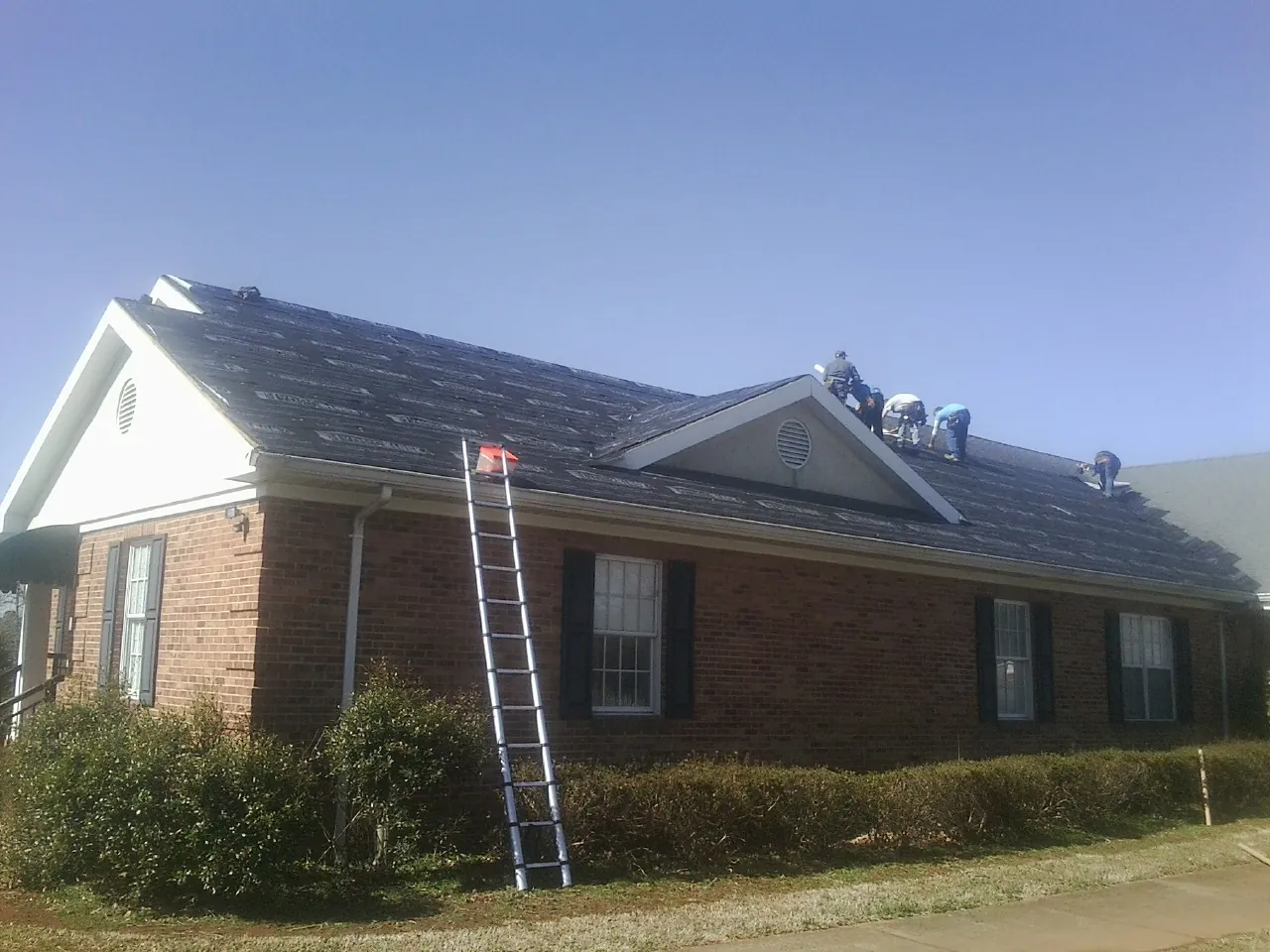 Crew tearing shingles off a brick ranch roof with a ladder set — Emergency Roof Repair work by our crew in Ahoskie