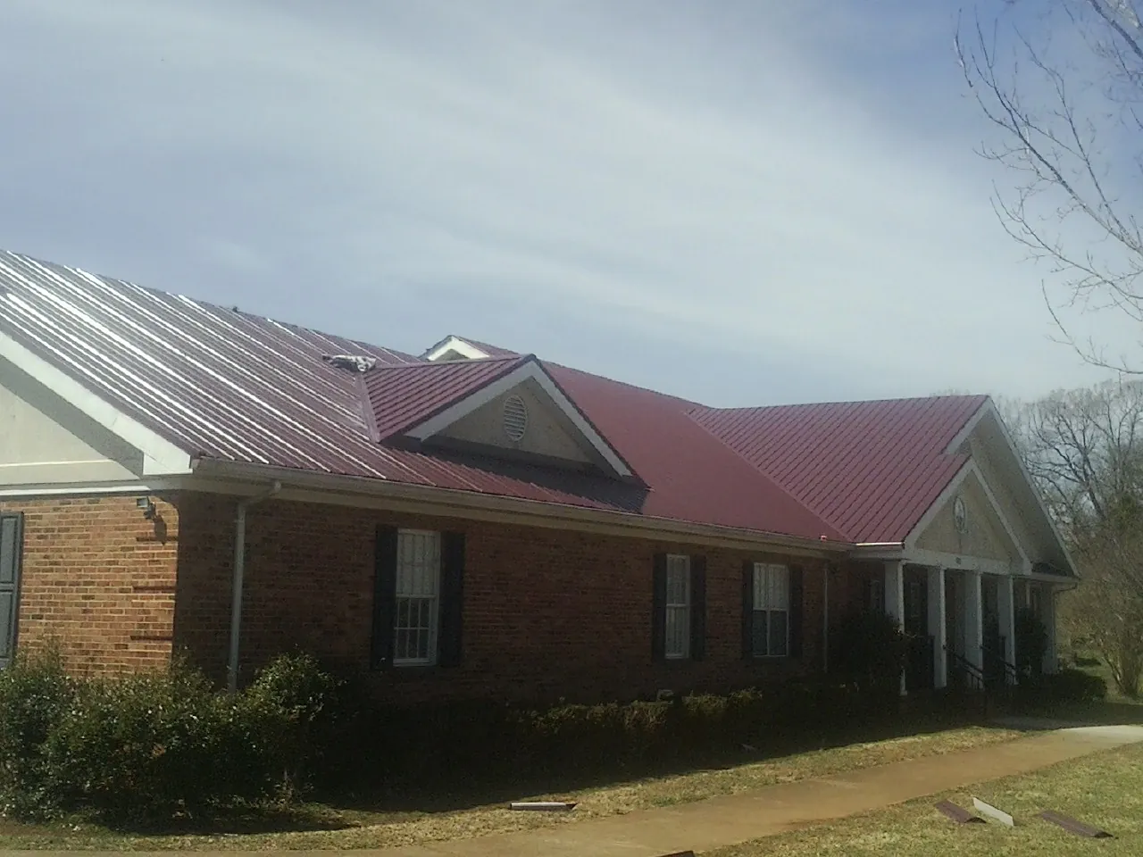 Red metal roof with gabled entries on a long brick building, from a Hail Damage Roof Repair job in Ahoskie