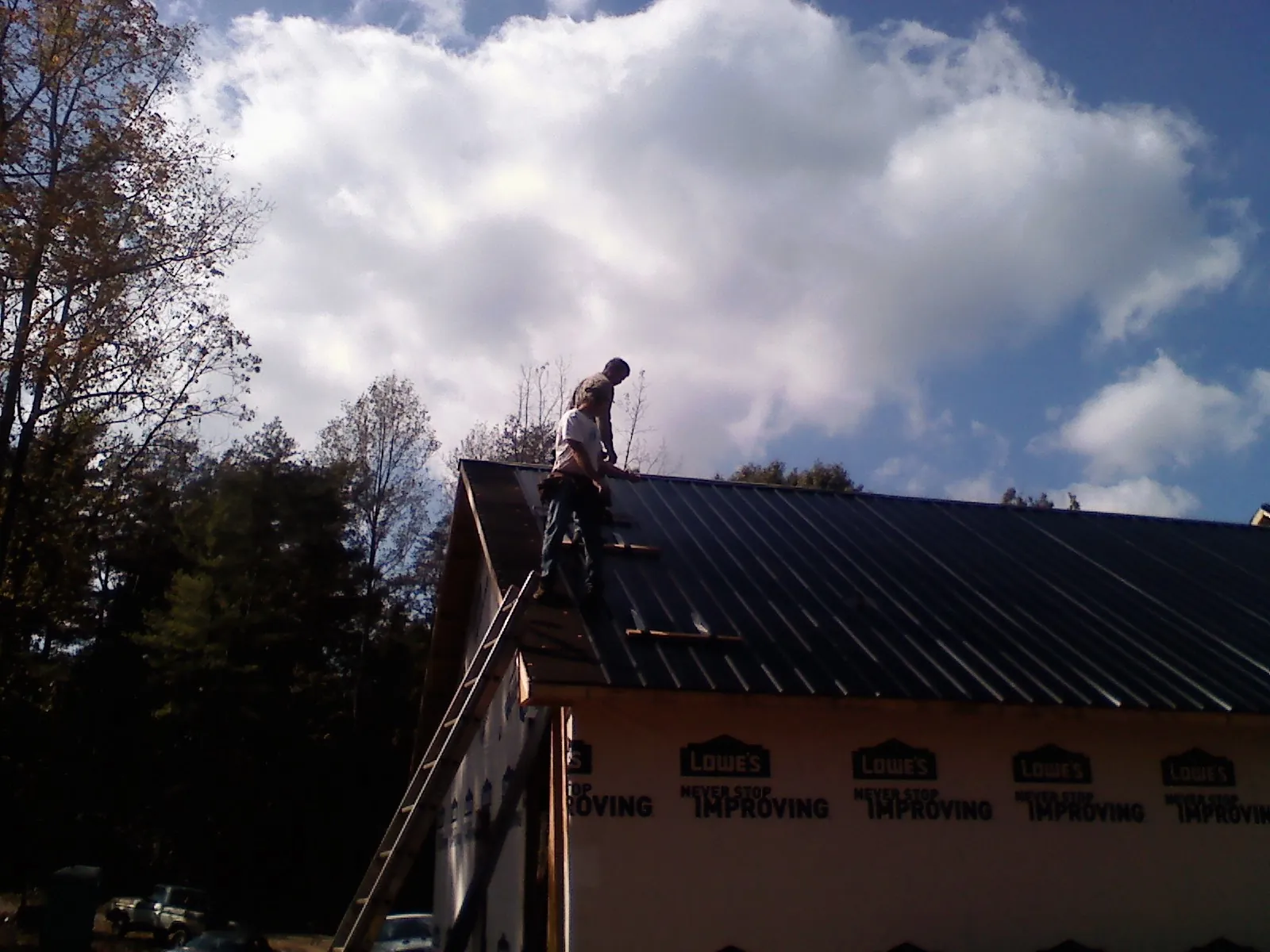 Roofer fastening dark metal panels high against a cloudy sky, from a Roof Inspection job in Ahoskie