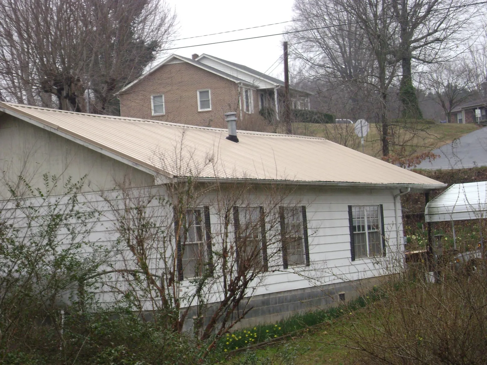 Tan metal roof on a white sided house set into a hillside — Commercial Roofing by Roofing Brothers in Ahoskie