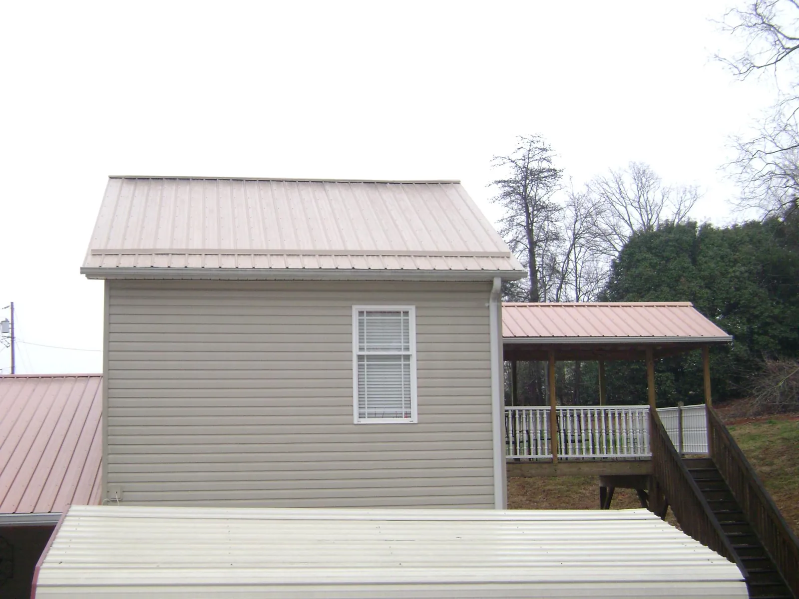 Tan metal roofs on a two story addition and attached porch, from a Roof Replacement job in Ahoskie